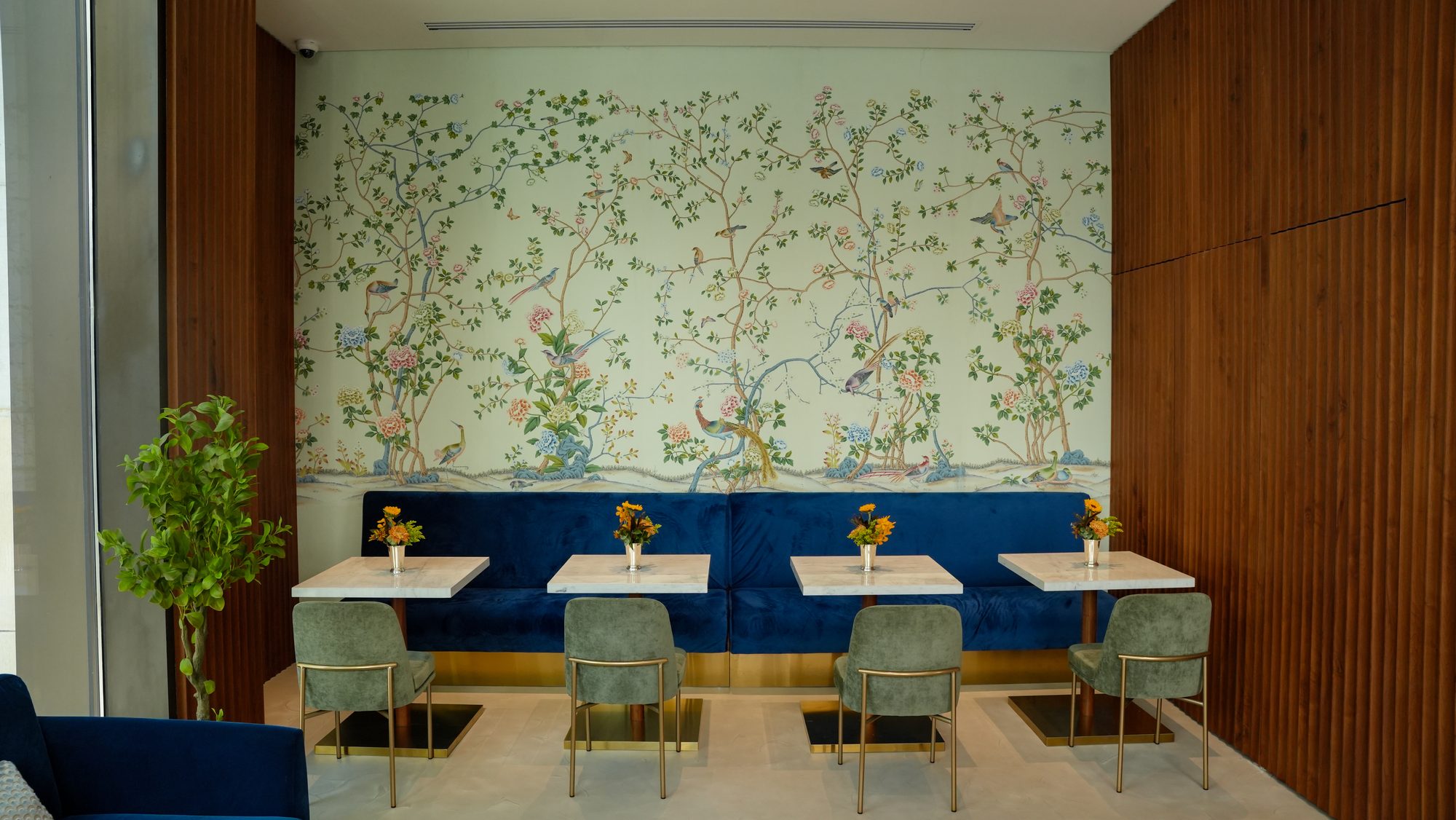 Vivel café blue velvet banquette seating with marble tables, hand-painted chinoiserie wallpaper and fluted walnut panelling